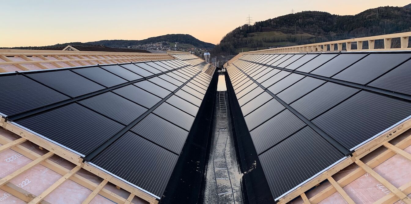 Solarpaneele auf einem V-förmigen Dach, eingebettet in eine hügelige Landschaft bei Sonnenuntergang. Solarpaneele auf einem V-förmigen Dach, eingebettet in eine hügelige Landschaft bei Sonnenuntergang.