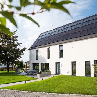 Ein modernes Haus mit Solarpaneelen auf dem Dach, umgeben von einem gepflegten Garten, unter klarem, blauem Himmel. Ein modernes Haus mit Solarpaneelen auf dem Dach, umgeben von einem gepflegten Garten, unter klarem, blauem Himmel.