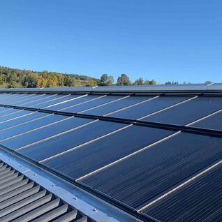 Solarpaneele auf einem geneigten Dach, umgeben von einer grünen Landschaft und blauem Himmel. Solarpaneele auf einem geneigten Dach, umgeben von einer grünen Landschaft und blauem Himmel.