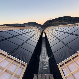 Solarpaneele auf einem doppelseitigen Dach im Bau, mit einer malerischen Landschaft im Hintergrund bei Sonnenuntergang. Solarpaneele auf einem doppelseitigen Dach im Bau, mit einer malerischen Landschaft im Hintergrund bei Sonnenuntergang.