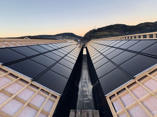 Solarpaneele auf einem V-förmigen Dach, eingebettet in eine hügelige Landschaft bei Sonnenuntergang.