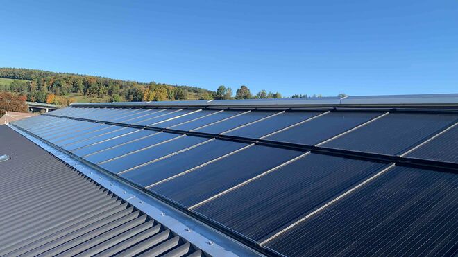 Solarpaneele auf einem geneigten Dach, umgeben von einer grünen Landschaft und blauem Himmel. Solarpaneele auf einem geneigten Dach, umgeben von einer grünen Landschaft und blauem Himmel.